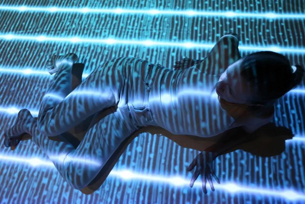 A person is lying on the ground with blue and white light patterns projected over their body and the background.